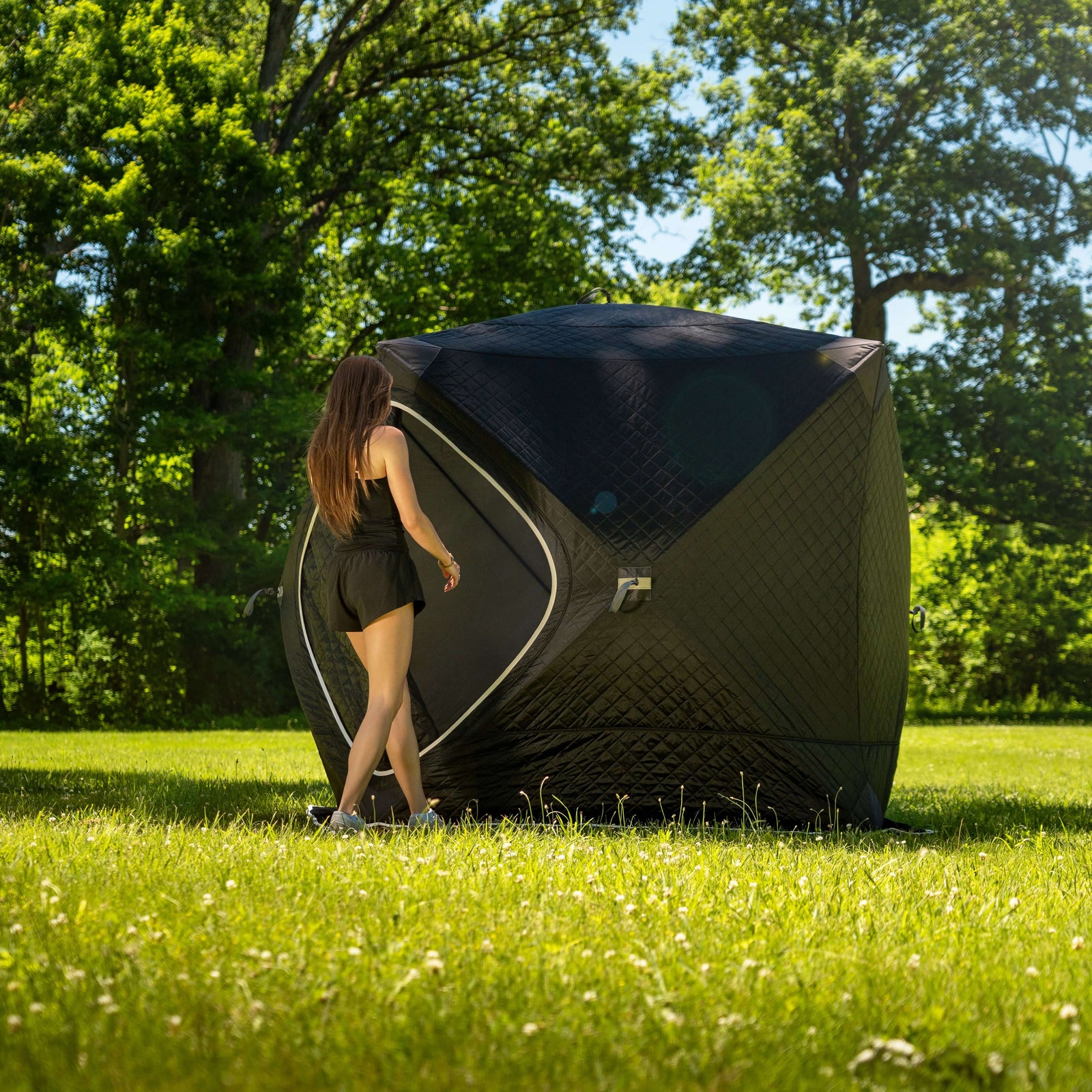 Person approaching the SaunaLife SaunaTrekker Portable Sauna Tent in a lush green setting.