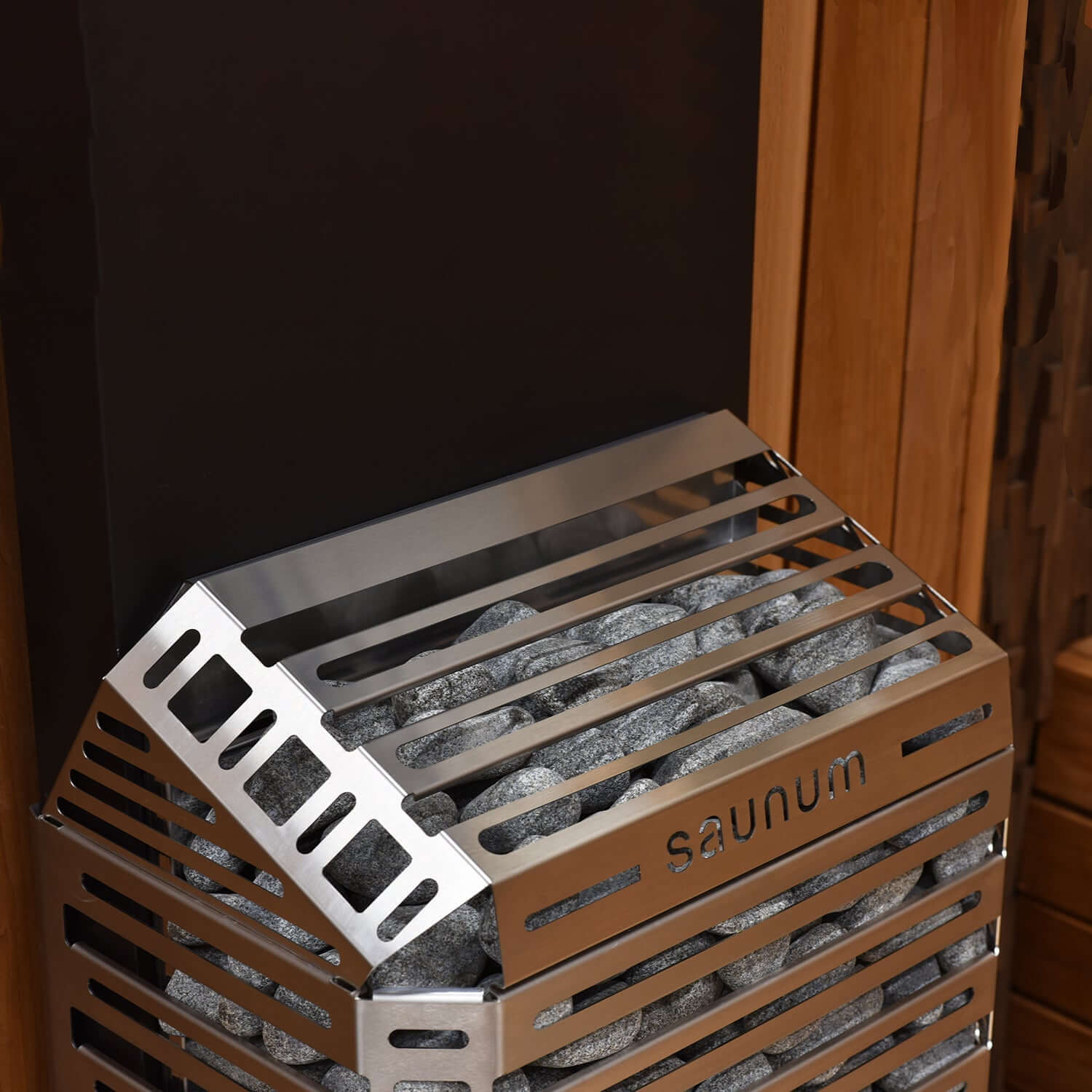 Metallic Saunum Air 5 electric sauna heater with stones inside, branded 'saunum', against a wooden background.