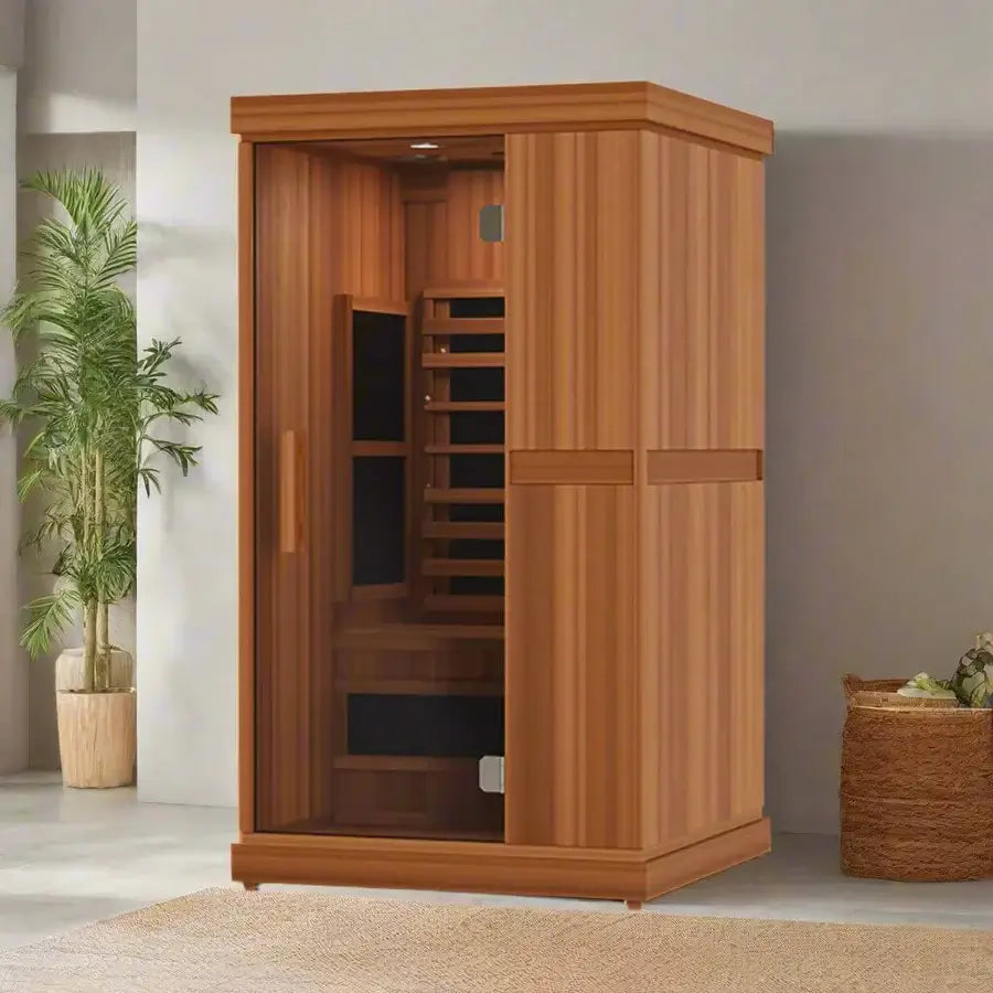 Wooden Finnmark FD-1 1-person full spectrum infrared sauna with a light brown wood exterior, featuring infrared heater elements, in a modern room with a plant, basket and carpet.