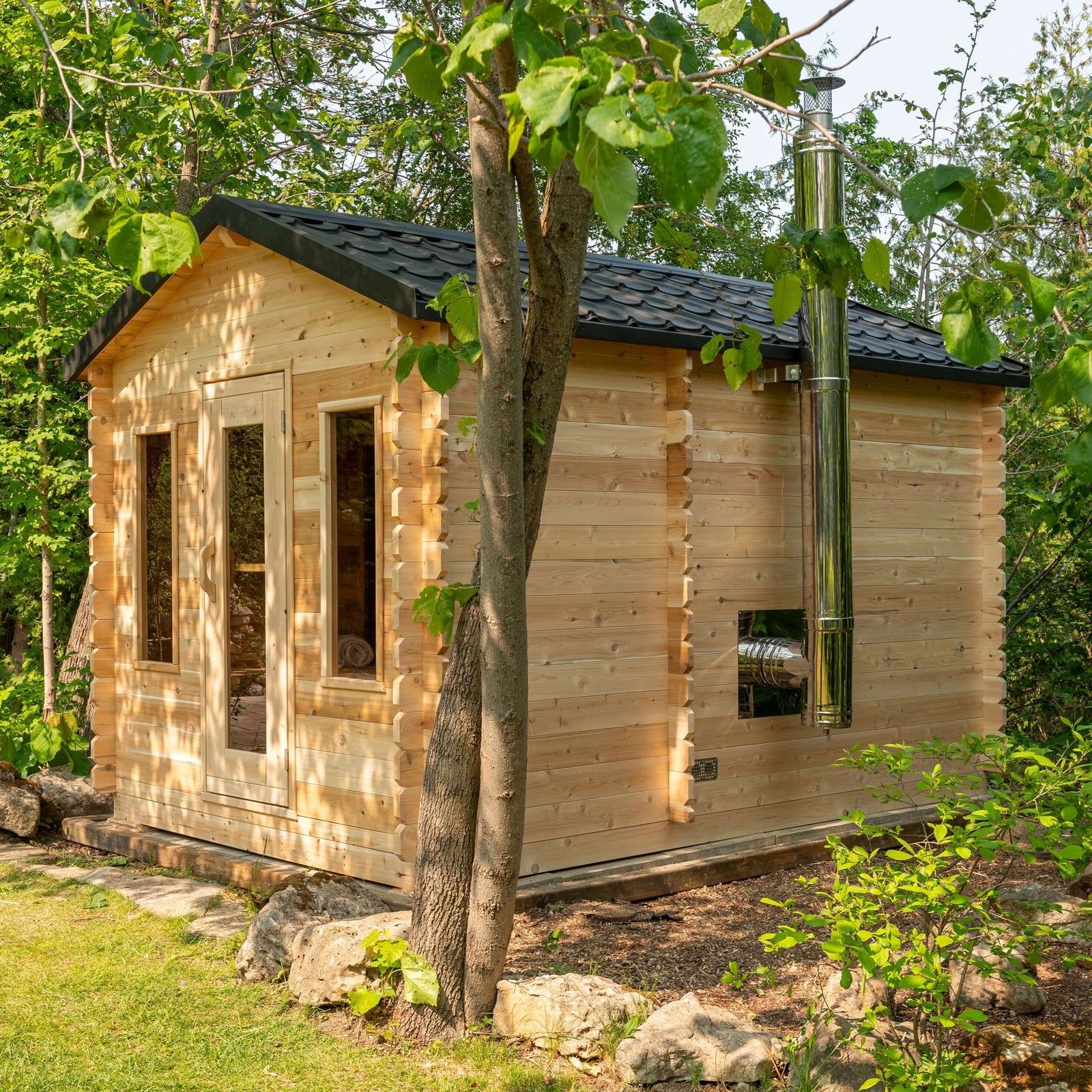 Dundalk Leisurecraft Canadian Timber Georgian Cabin Sauna with Changeroom made of eco-friendly white cedar wood in a lush outdoor setting. CTC88CW
