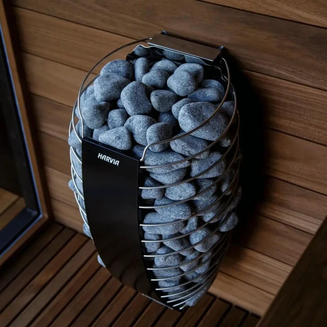 Harvia Spirit electric sauna heater with visible stones inside mounted on a wooden wall, a wooden floor can also been seen