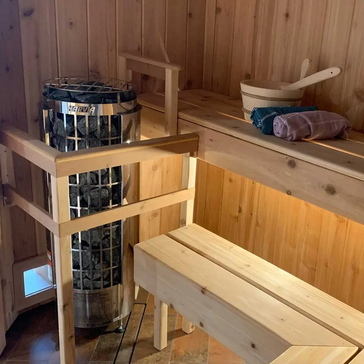 Wooden sauna interior with a Harvia Cilindro Half Series Electric Sauna Heater with it's exposed sauna stone column cylinder, benches, and towels.