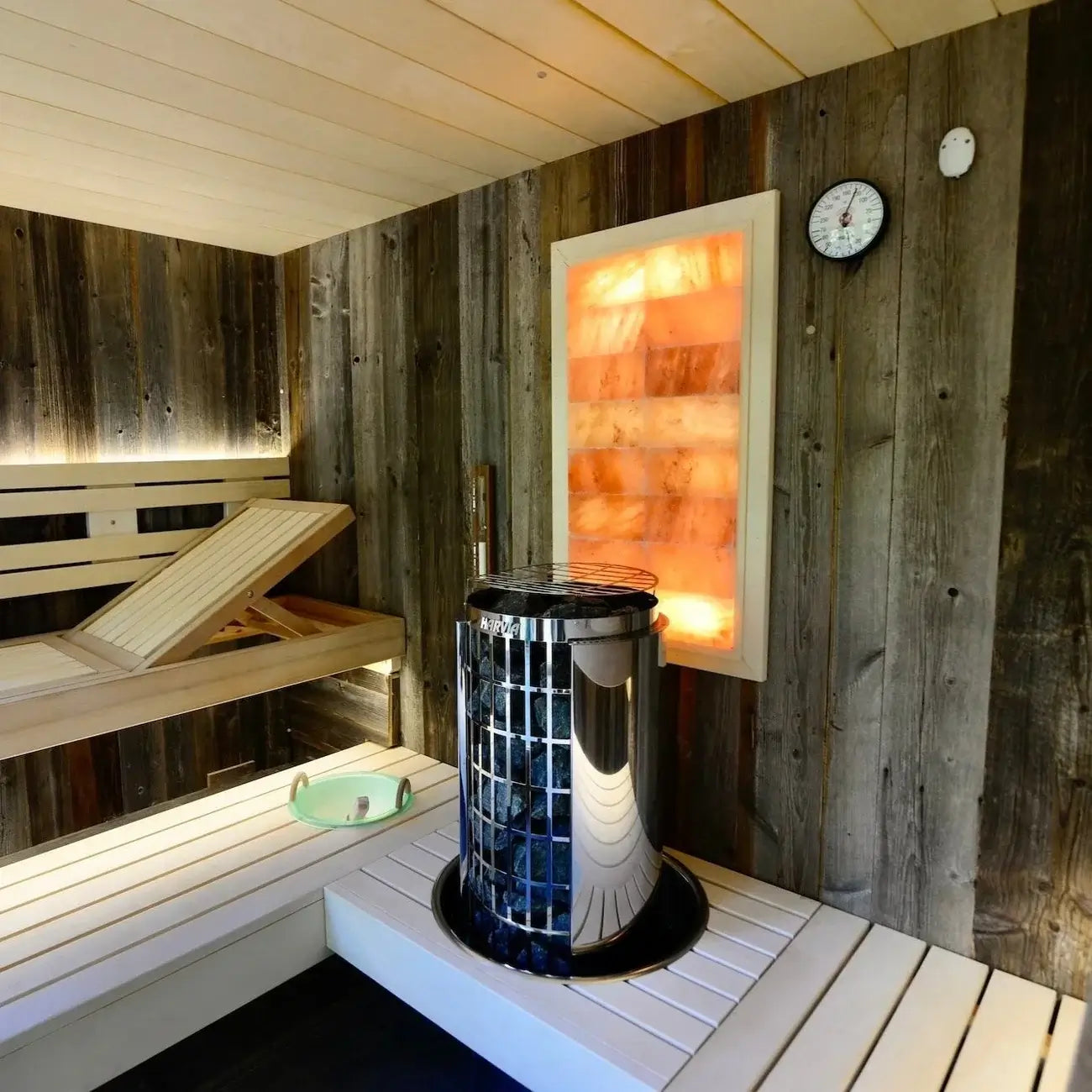 Sauna room with wooden benches, a Harvia Cilindro Half Series Electric Sauna Heater and a wall-mounted light fixture.