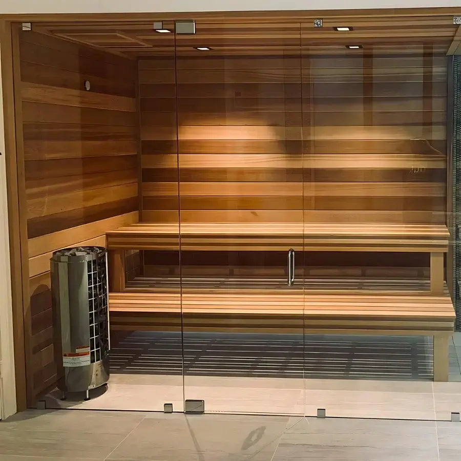 A wooden sauna with a full glass front wall and door, featuring multiple tiers of wooden benches, and a stainless steel Harvia Cilindro electric pillar heater placed on the left side along the wall.