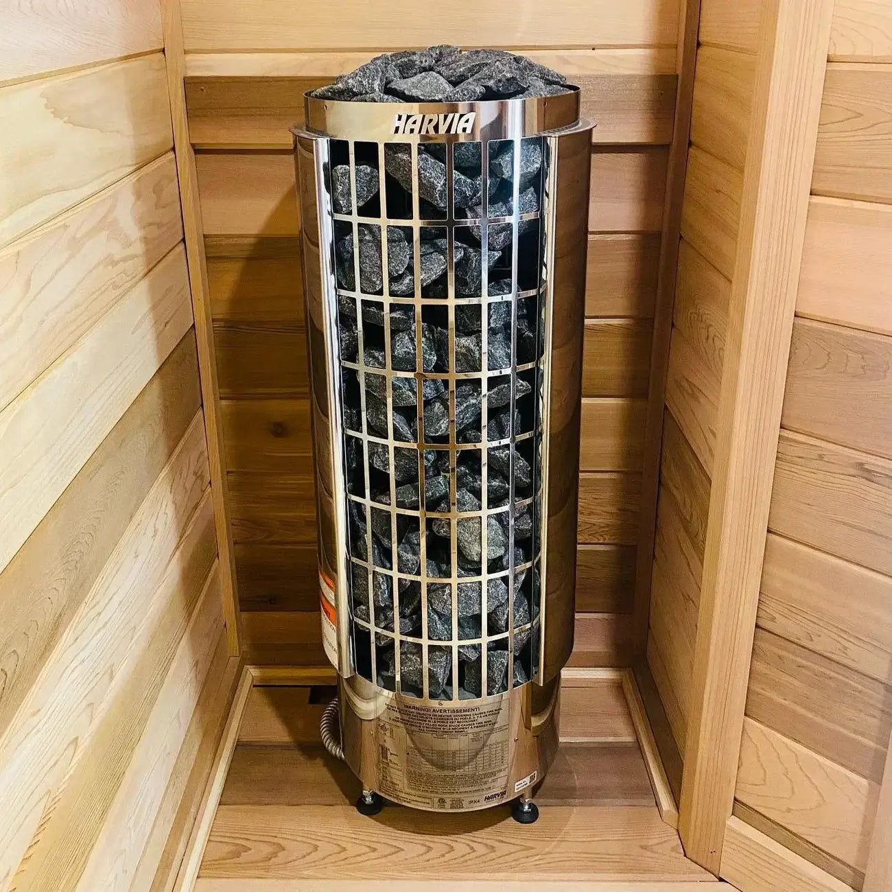 A cylindrical Harvia Cilindro Half Series Electric Sauna Heater filled with dark heating rocks, set inside a wooden sauna room.