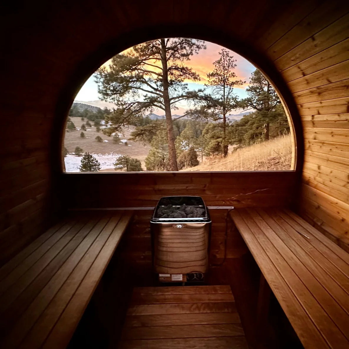 Wooden sauna with a large round window overlooking a scenic landscape and Harvia KIP with built in controls sauna heater.