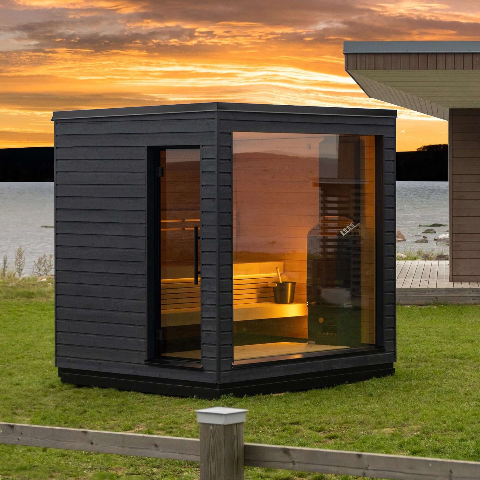 SaunaLife G6, an outdoor sauna with glass walls in a grassy area during sunset.