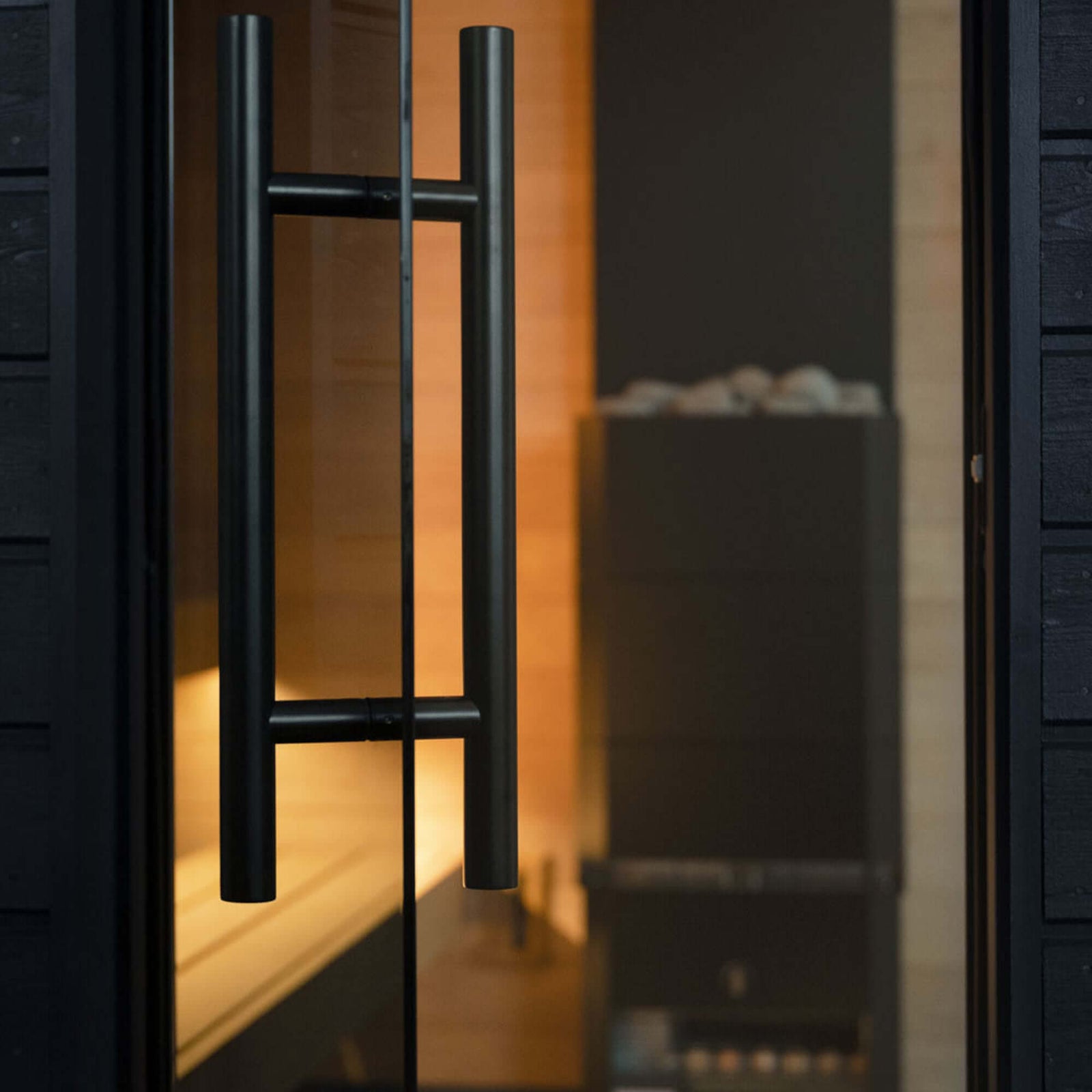 Close-up of SaunaLife's G6 sauna's black door handle on a glass door with a blurred interior background