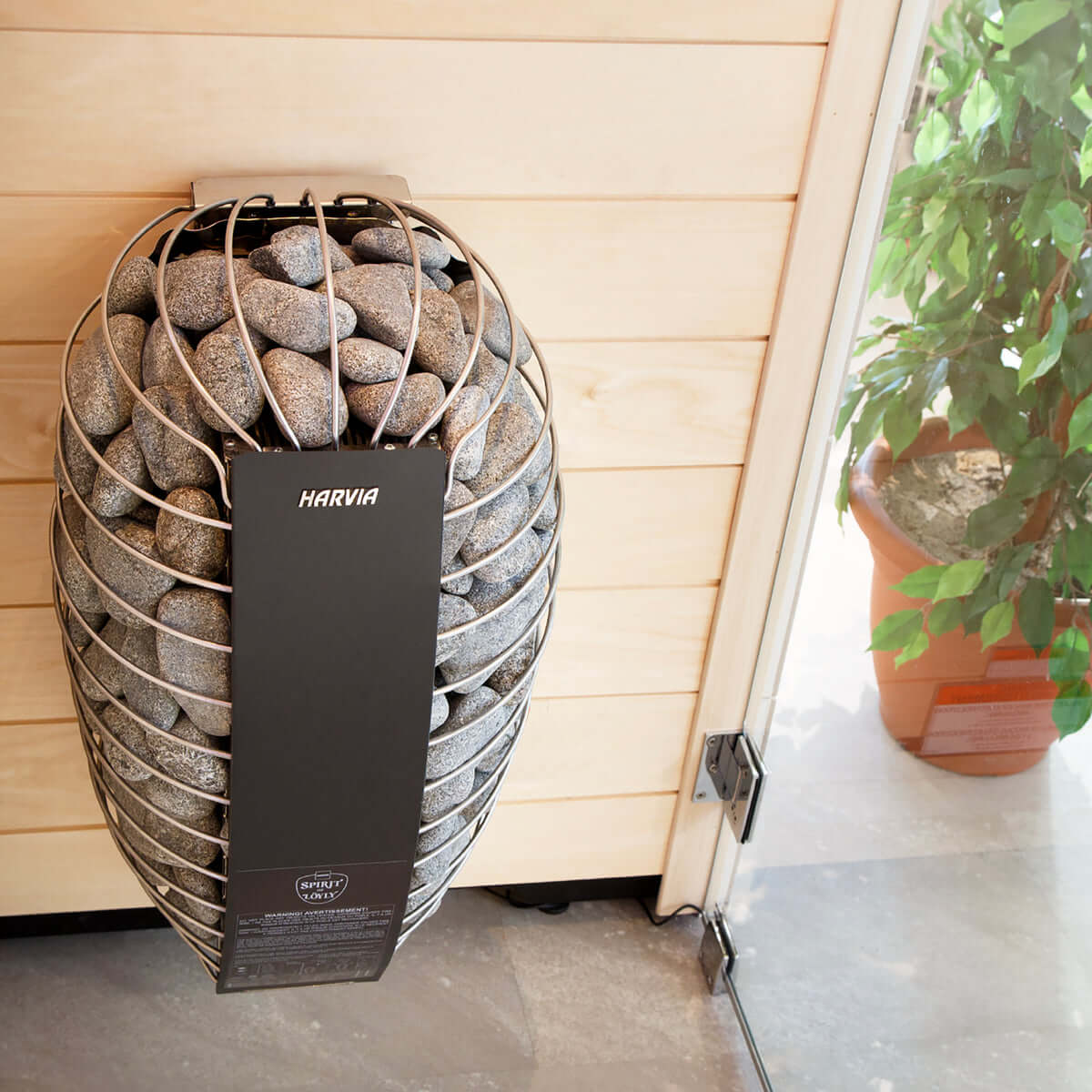Harvia Spirit electric sauna heater with stone design in a sauna room with window door and a plant