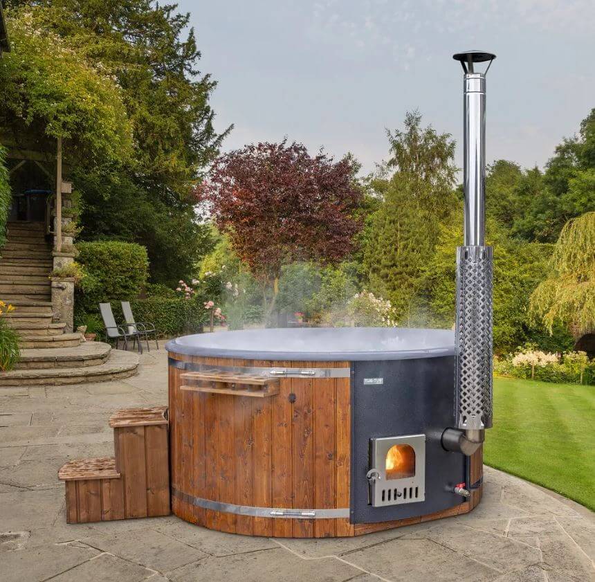 SaunaLife S4N wood-fired hot tub in a garden setting with trees and a stone pathway.
