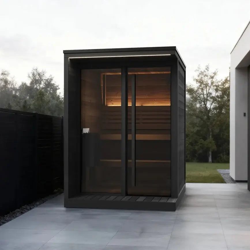 SaunaLife's GL4GB, a modern outdoor sauna cabin with dark wood framing, a large glass door and window, set on a paved patio next to a contemporary house.