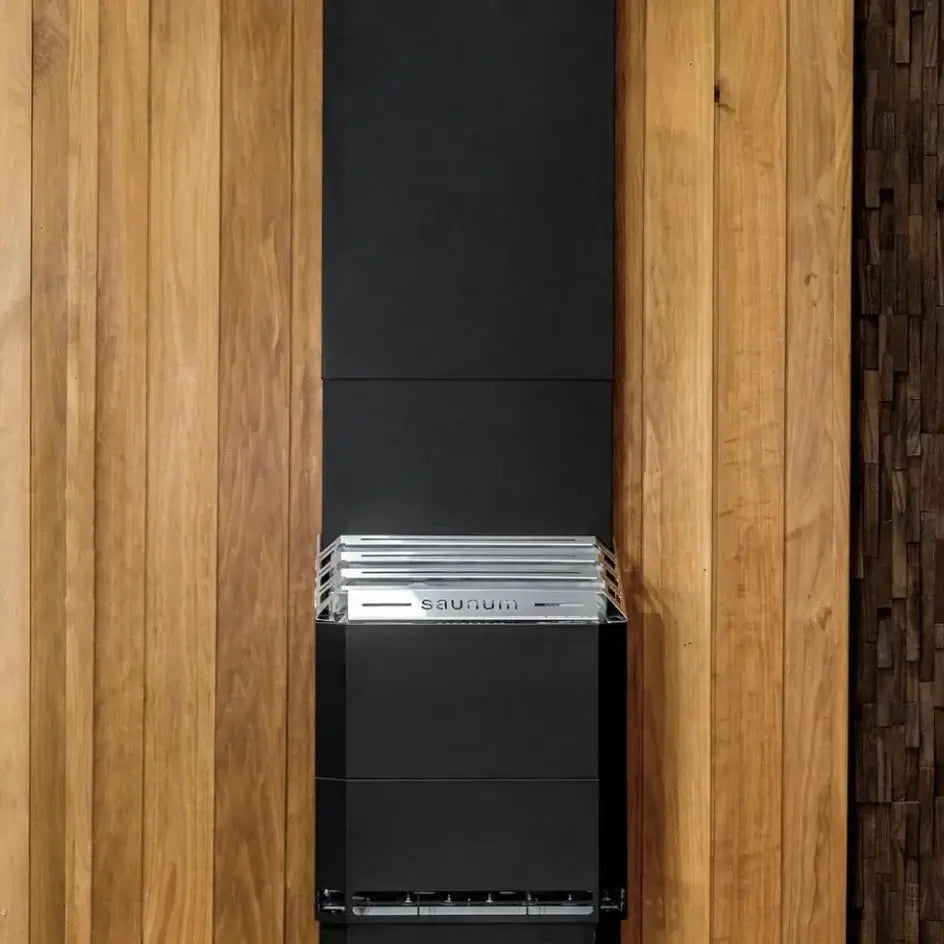 A modern black and silver Saunum AIR 5 sauna heater with closed stone basket
mounted on a vertical wood-paneled wall.