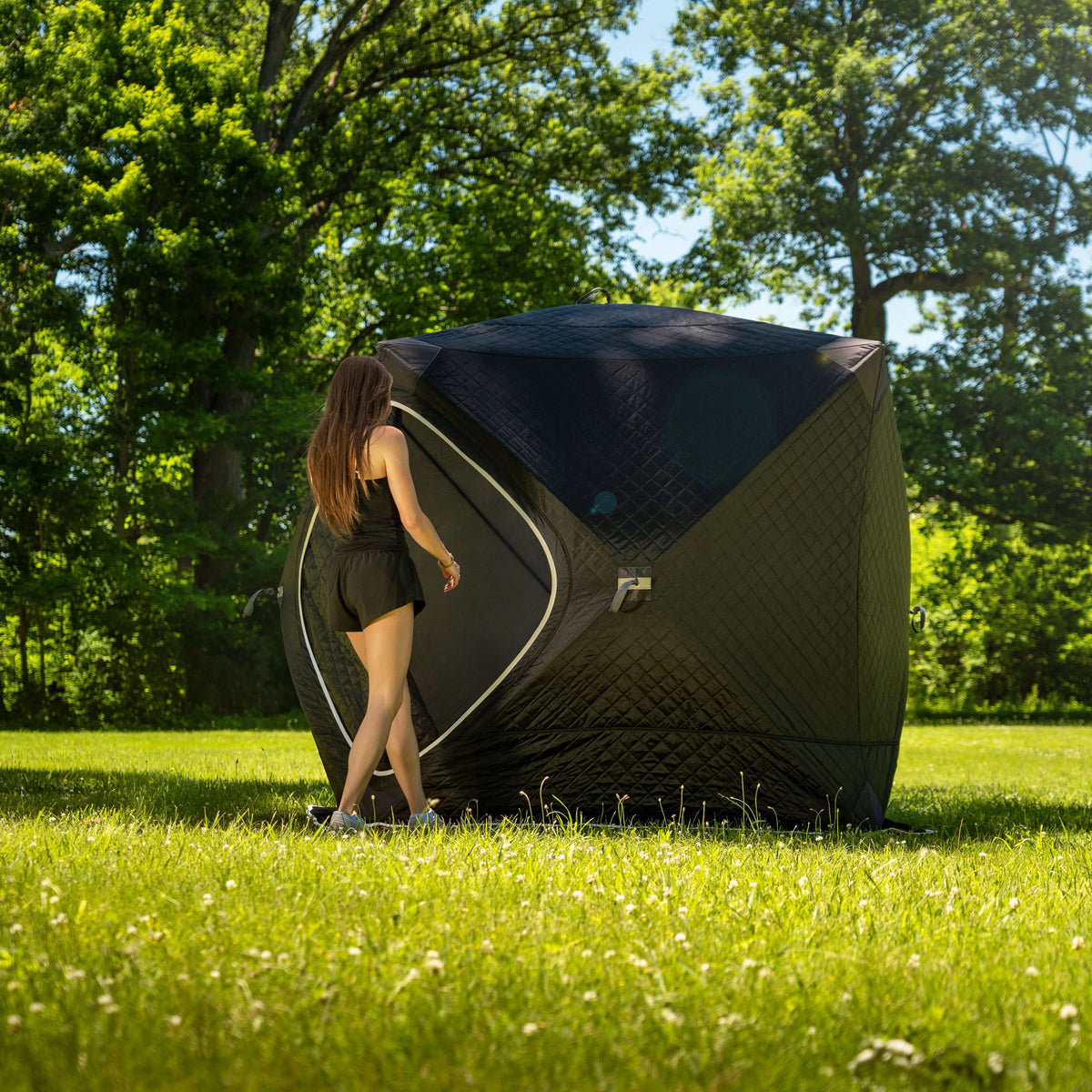 Person approaching the SaunaLife SaunaTrekker Portable Sauna Tent in a lush green setting.