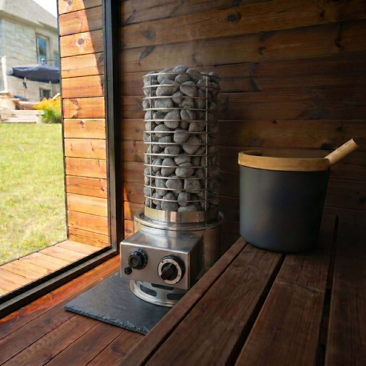 SaunaLife TITAN SL1 Portable Propane Sauna Heater with sauna stones and wooden bucket in a rustic setting.