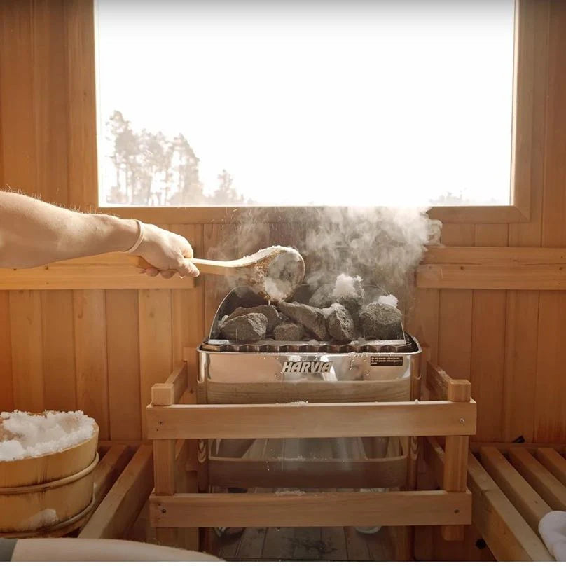 Person inside a sauna, using a ladle to poor water on hot stones of the Harvia KIP sauna heater.