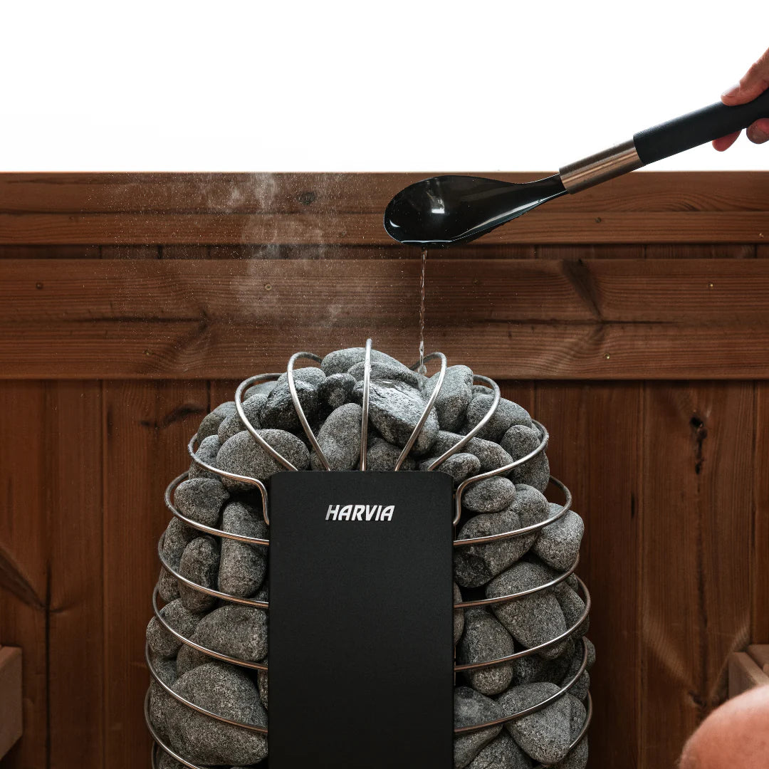 Harvia spirit sauna heater with a person using a ladle to put water on the stones, in a wooden sauna.