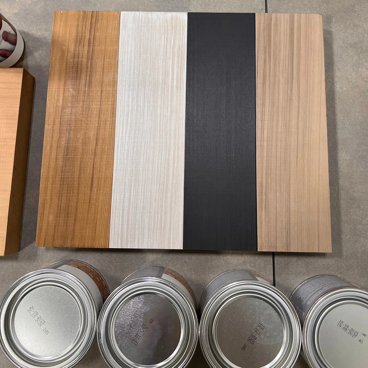 Wooden panels with different finishes and a row of paint cans on a gray surface.
