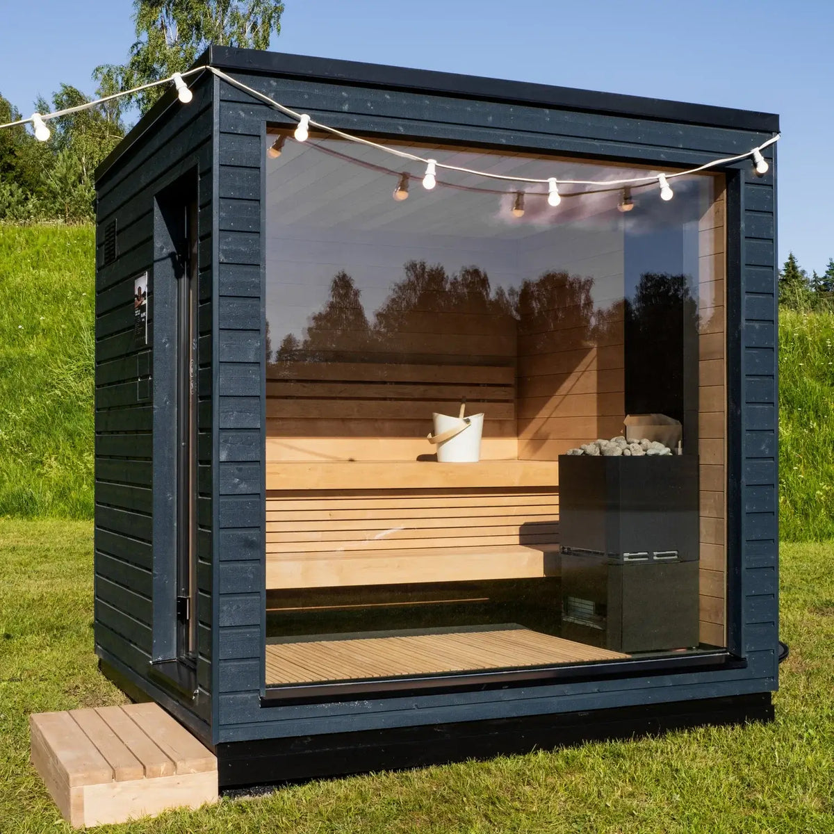 Outdoor SaunaLife G6 sauna with black -painted exterior and wooden interior, surrounded by greenery.