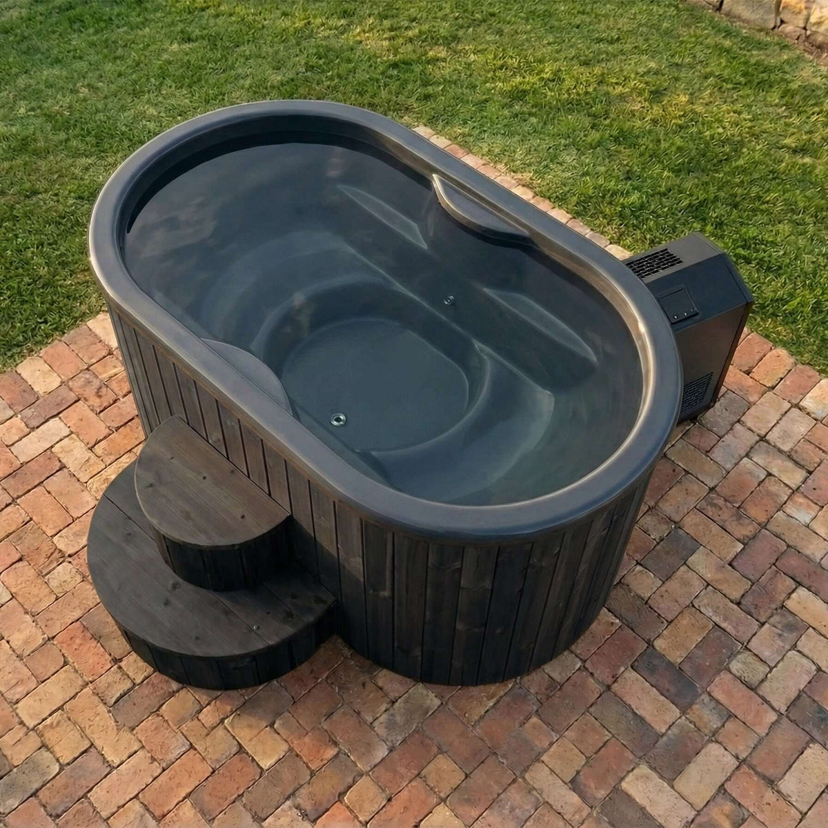 Saunalife s2b black cold/hot plunge tub made of thermo-pine wood with matching black stairs, designed for two persons, on a brick patio with grass in the background 